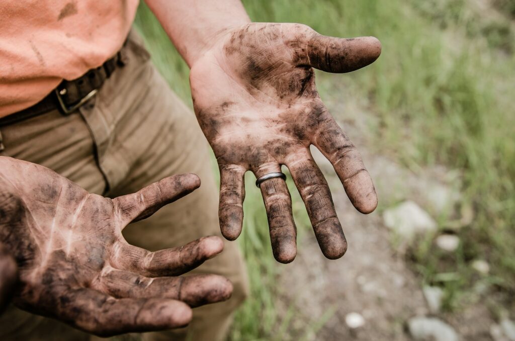 A person with soil-covered hands, suggesting manual work or gardening.